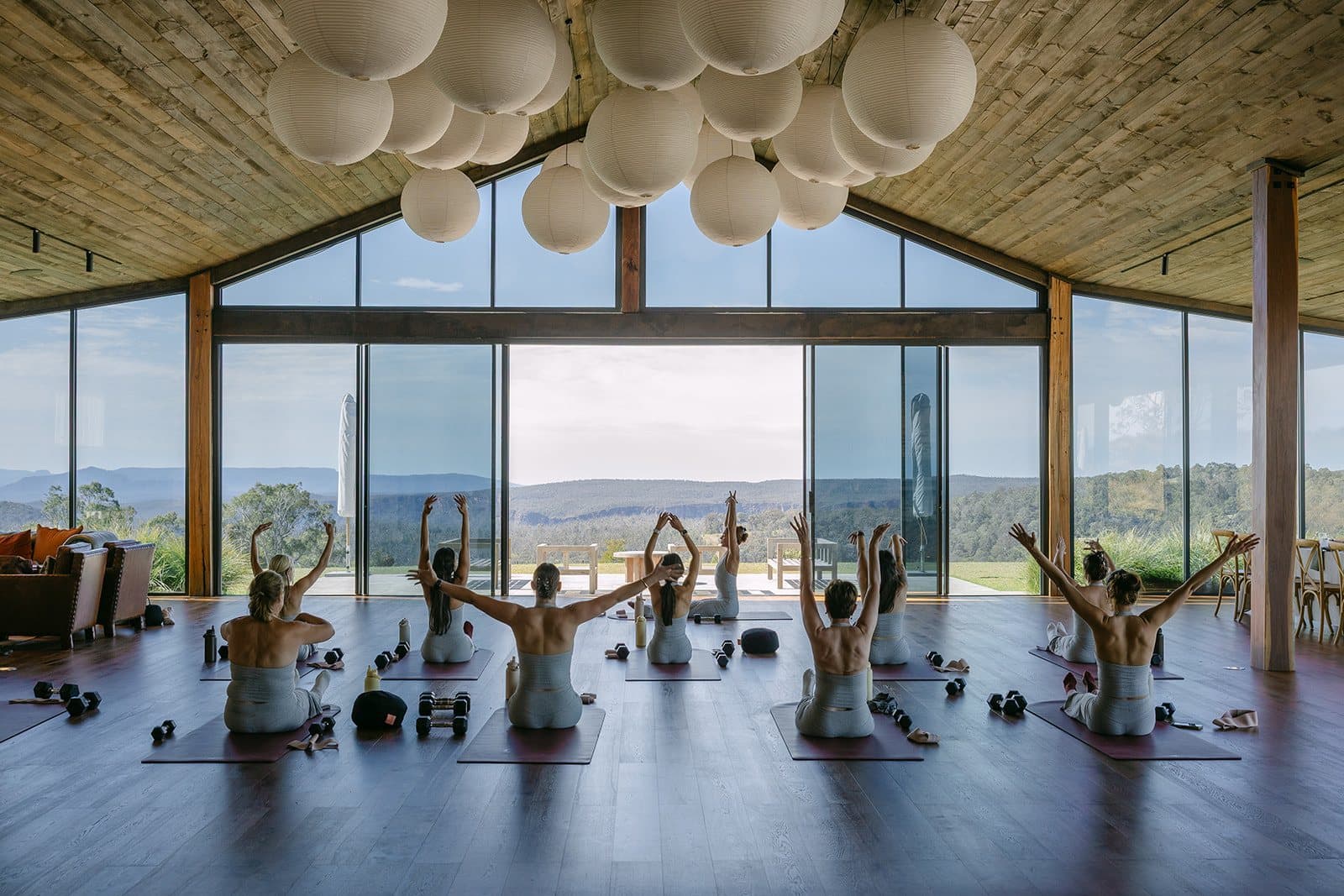 A retreat group kneeling on mats in the Pavilion with their arms raised, the ranges through the gabled glass in front of them