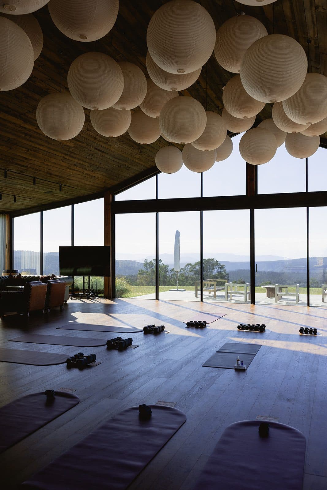 The Pavilion floor laid out in rows of mats and hand weights for a morning retreat session, the escarpment through the glass beyond