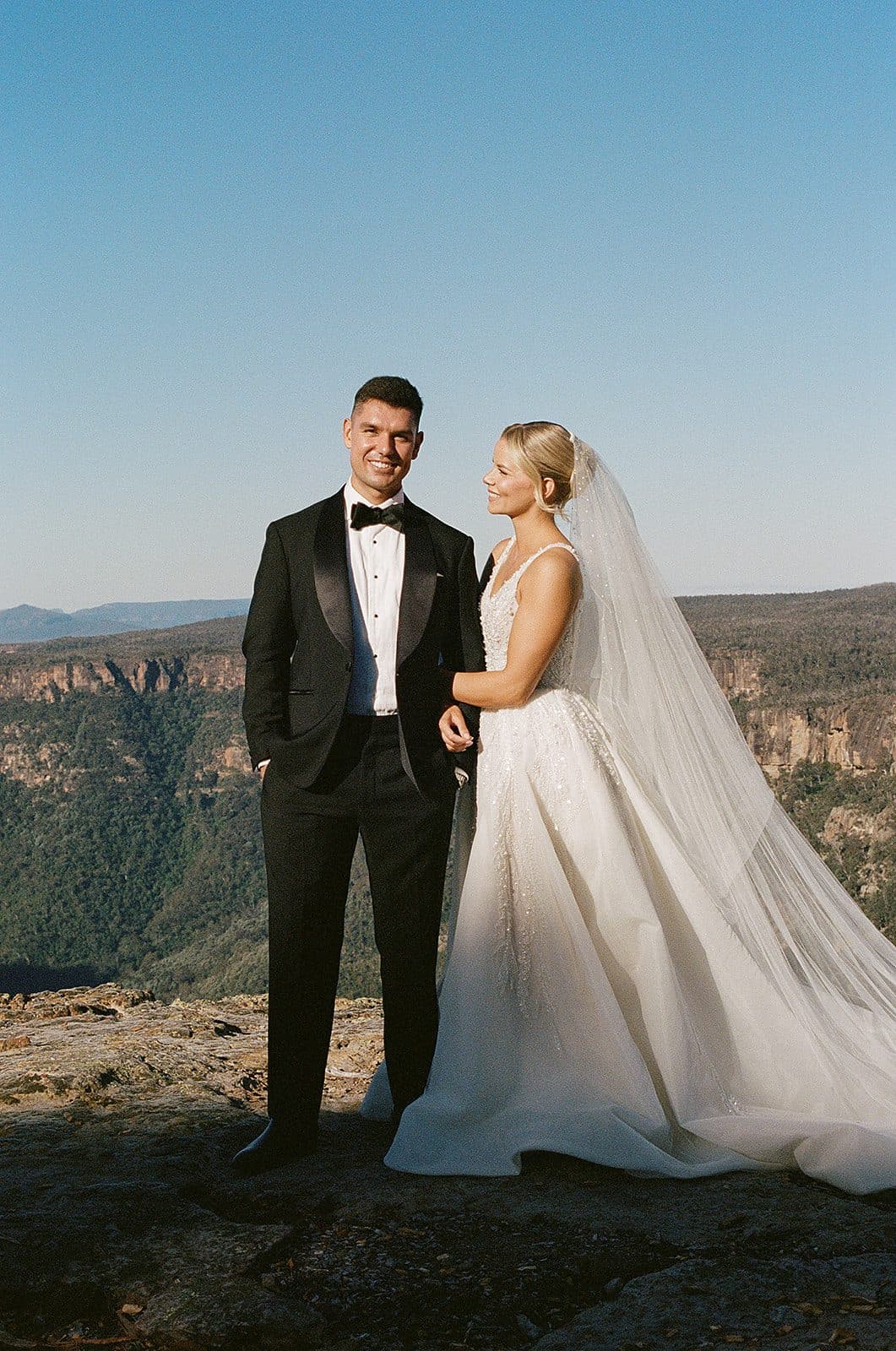 A newly married couple standing hand in hand on the rock at the cliff edge, the gorge and escarpment behind them