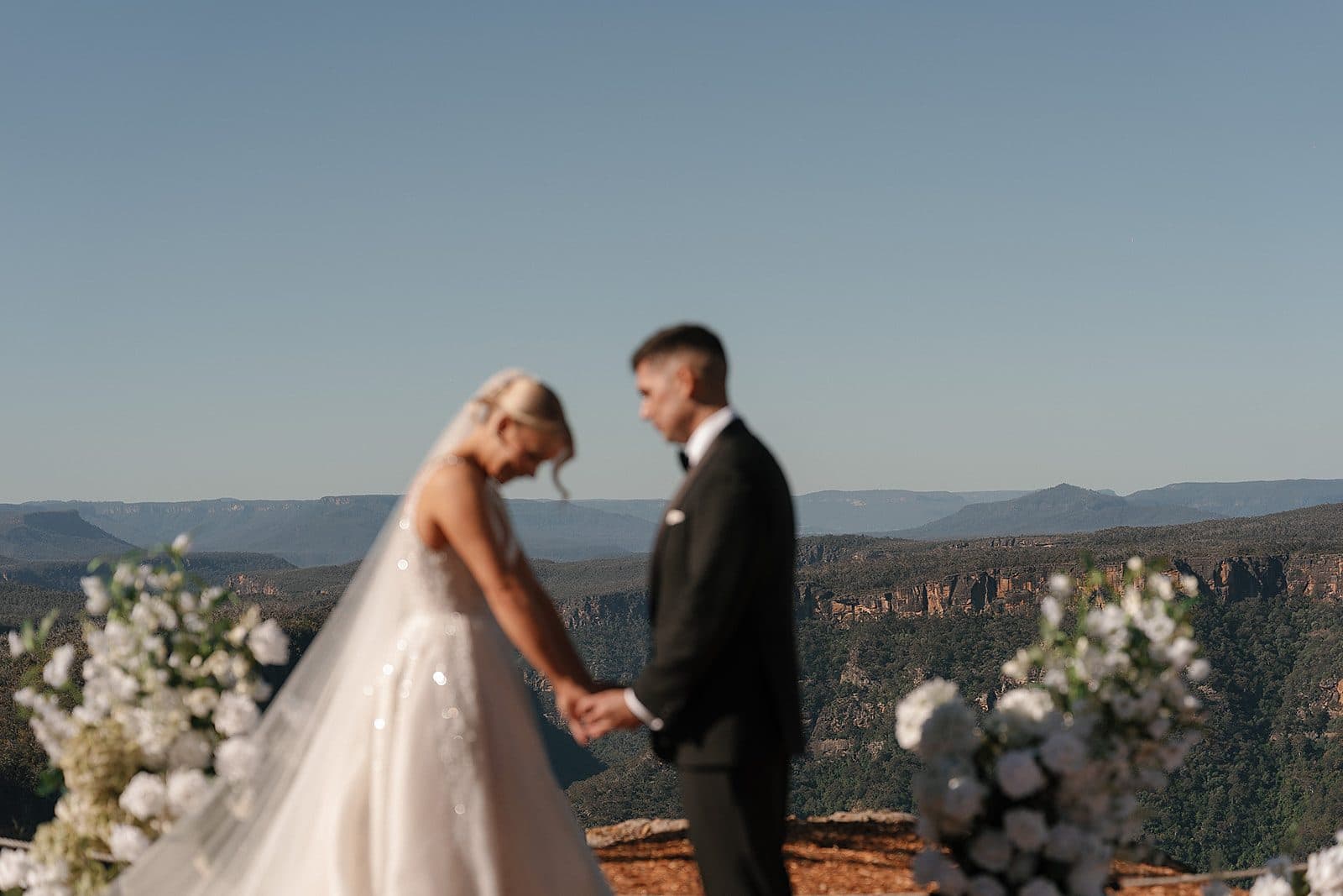Lauren and Corey holding hands at the edge of The Cliffs, white florals either side and the gorge behind them