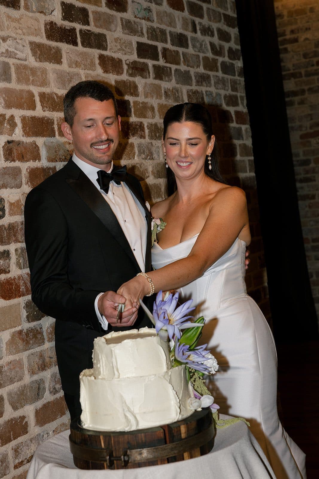 Matt and Holly cutting the cake against the brick wall