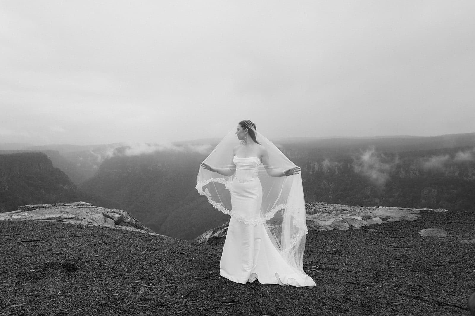 Holly alone at The Cliffs, her veil held wide, cloud pouring through the gorge behind her