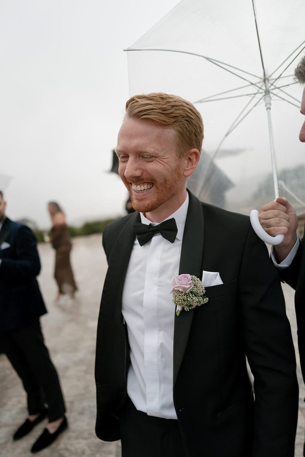 A guest laughing under a clear umbrella on the terrace, the ridge behind him lost in cloud