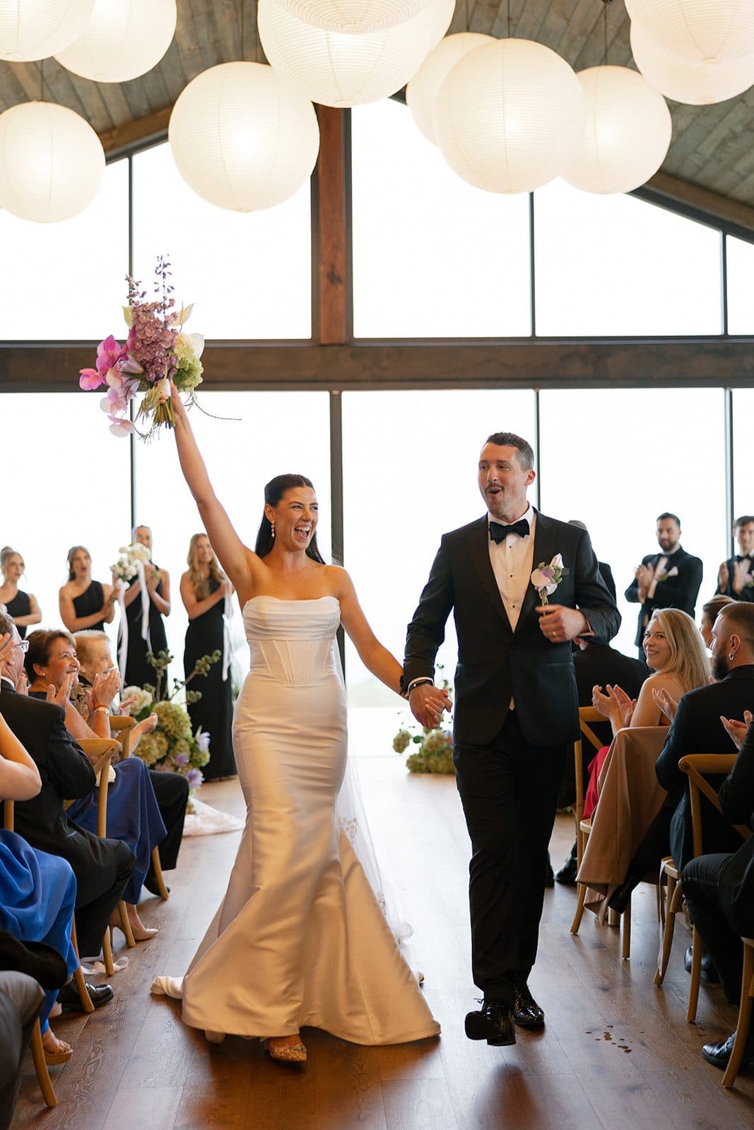 Holly and Matt coming back down the aisle under the lanterns, guests standing either side